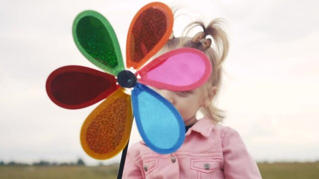 little daughter girl play pinwheel a wind toy. happy family concept. child plays with windmill. portrait girl blonde lifestyle kid holds flower toy spinning pinwheel. happy childhood