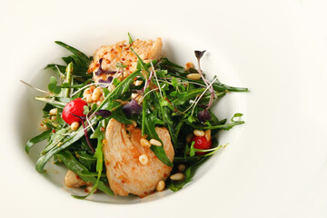 salad with chicken arugula and pine nuts closeup in white plate on grey concrete background
