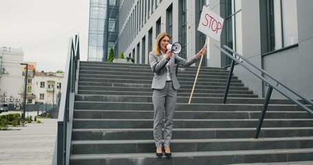 Single protest of Caucasian woman in glasses talking and screaming in megaphone. Female protestant holding table Stop while bringing attention to political or environmental issue. Lonely protestation.