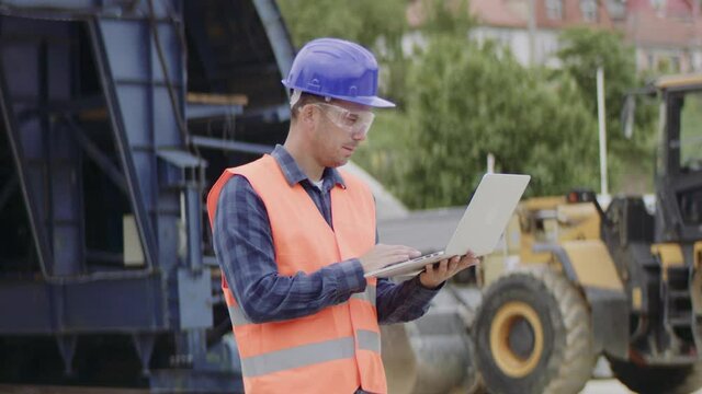 Construction engineer or a supervisor with a halmet and protective equipment on a building construction site using a laptop.