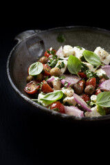 Salad with Olives, Cherry Tomatoes, Feta Cheese and fresh Basil on black Stone Background. Healthy Snack Idea. Close up. Copy space. 