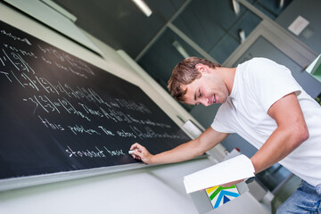 Handsome college student solving a math problem during math class in front of the blackboard/chalkboard (color toned image)