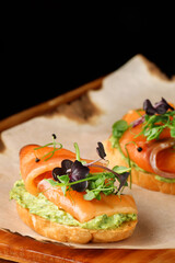 bruschetta with salmon closeup. tapas with salmon on guacamole and topped microgreen on wooden board and black background
