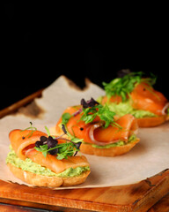 bruschetta with salmon closeup. tapas with salmon on guacamole and topped microgreen on wooden board and black background