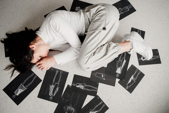 Woman designer laying in an embrion pose with her sketches around