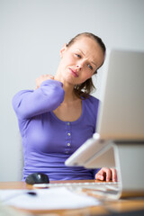 Working too hard - young woman working on a computer at an office, having sore back, being overloaded with work, sitting too much, putting too much stress on her eyes,..