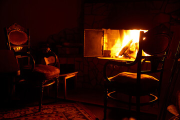 Fireplace with fire and old chairs in a dark room