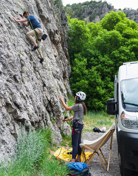 Girl belaying man up rock wall.