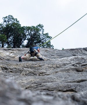 Man climbing up rock wall with rope and harness