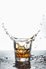 Rocks glass with whiskey in which ice drops splashing on a bar counter. Light background. Copy space