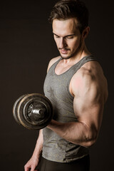 Portrait of an attractive muscular athlete with dumbbells on a dark background