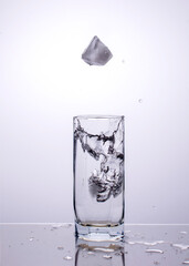 Ice cubes fall into a glass with splashes of water.