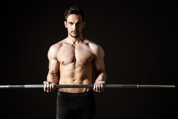 Portrait of a handsome muscular man posing with a barbell on a dark background