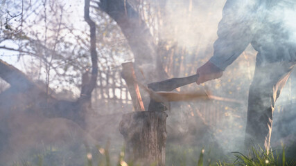 Worker chopping wood outdoors. An axe cuts through a wooden log in haze