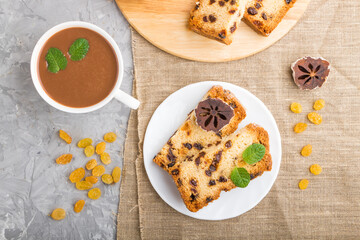 Homemade cake with raisins, dried persimmon and a cup of hot chocolate on a gray concrete background. top view.