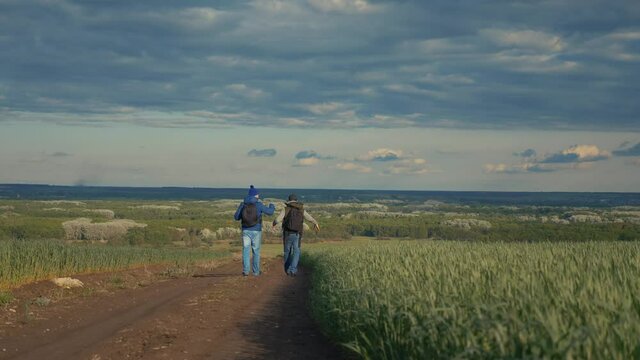 teamwork travel. two man hikers with backpacks walk along a trail next to a field with green grass in nature. concept adventure travel hiking healthy. lifestyle two tourists walk walking talking