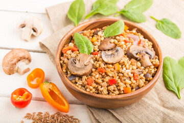 Spelt (dinkel wheat) porridge with vegetables and mushrooms in wooden bowl on a white wooden background and linen textile. Side view, selective focus.