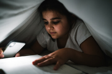 girl reading under the sheets with a flashlight