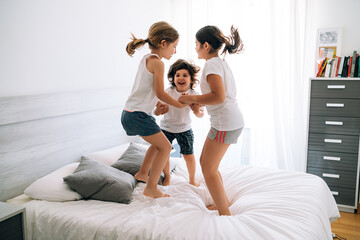 three siblings jumping into bed holding hands in fun ways