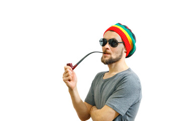 Young caucasian smoker man in rasta hat, sunglasses and grey t-shirt on white background with smoke...