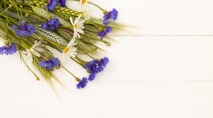 Spikelets, cornflowers and daisies on white wooden background. Top view. Copy space. Banner