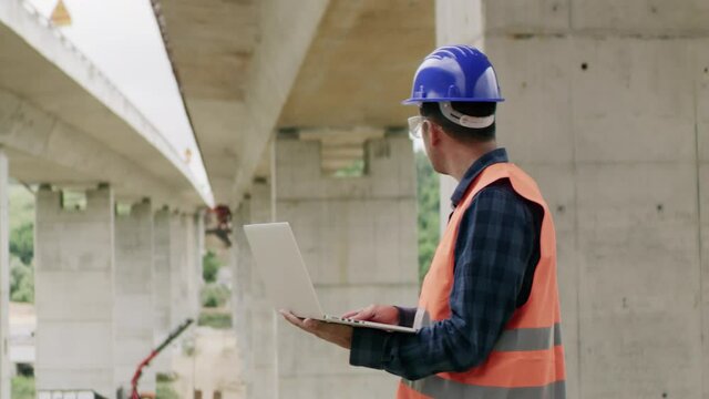 Construction engineer or an architect with a halmet and protective equipment on a building construction site using a laptop.