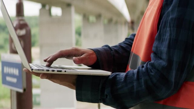 Construction engineer or an architect with a halmet and protective equipment on a building construction site using a laptop.