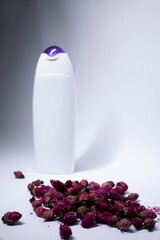 white shampoo bottle with purple neck and no label near a pile of little pink roses. body care and...