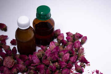 little liquid bottles with no label near a pile of little pink roses. body care and beauty concept. Copy space. High quality photo