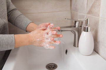 A woman washes her hands with soap over a washstand under a jet of running water. Bathroom. 