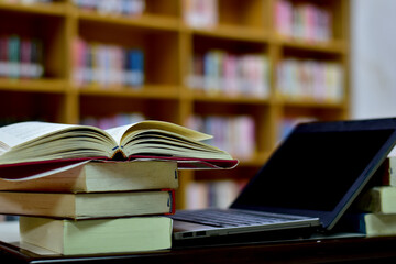 Fototapeta premium Stack of books with laptop on table in library, image selective focus and blurred bookshelf in the library, education background, back to school concept.