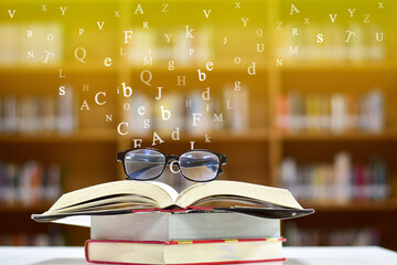 Glasses placed on open books on wood table and English alphabet Floating above the book in the library and blur bookshelf background.