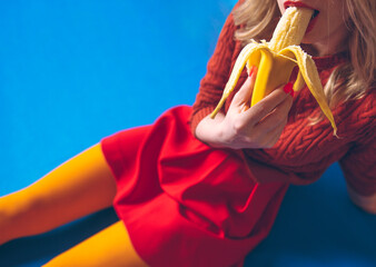 girl in yellow tights and a red skirt is sexy eating a banana on the blue floor