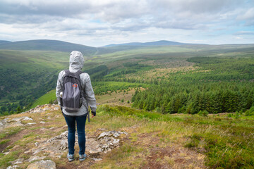 Girl (hiker) is looking at panoramic Guinness Lake (Lough Tay) valley -  a movie and series location, such as Vikings. Close to Dublin City, popular tourist destination.