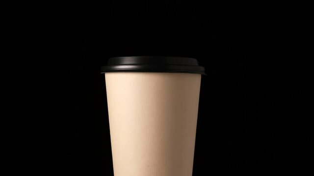 brown cardboard glass with a plastic lid rotates around its axis on a black background, disposable tableware