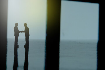 Fototapeta na wymiar Silhouette of two businessmen make an handshake partnership agreement. Miniature people figure conceptual photography