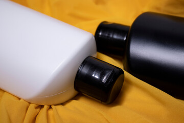 Composition of a black and white shampoo bottles with no label in a silk yellow fabric. body care and beauty concept. Copy space. High quality photo
