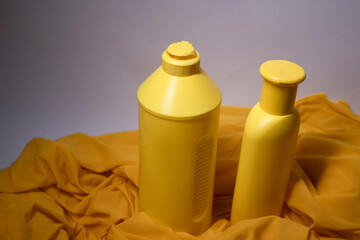 Composition of two yellow shampoo bottles with no label in a silk yellow fabric. body care and beauty concept. Copy space. High quality photo