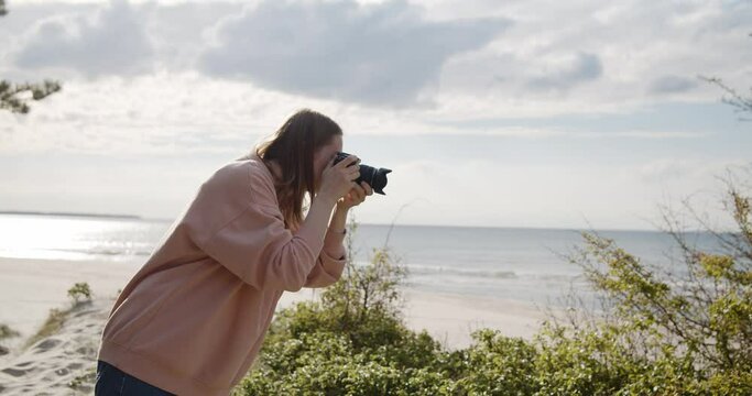 Young woman photographer takes pictures of the sea using digital camera