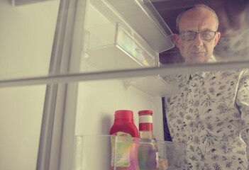 Portrait of a hungry senior man looking for food in refrigerator. Eating and diet concept -...