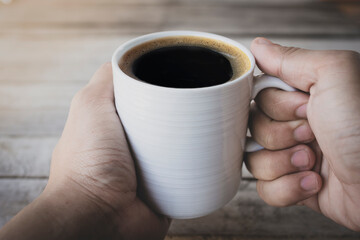 close up of a man with a black coffee cup in a wooden background.