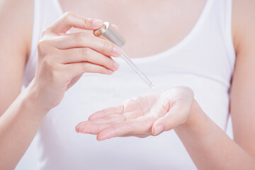 Pipette with drop of essential oil and bottle in woman hands on beige textile.