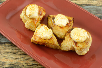 Boneless chicken breast pieces with sour cream and red pepper pesto sauce on top on red dinner meat platter