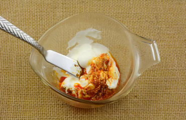 Mixing red pepper pesto sauce and sour cream in glass measuring cup with butter knife