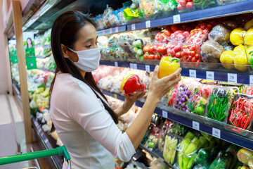 Asian woman wearing protective face mask push and hold shopping cart in supermarket department store. Girl, looking grocery to buy  some food. New normal after covid-19. Family concept.