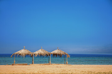 Three sunshades, made from palm leaves on the beach of the Red Sea