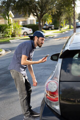 A view of a man holding a cell phone looking into the driver's side of a car, acknowledging to the...