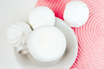 Cup of cappuccino and white zephyr on white and pink background close up