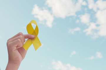 Hands holding yellow gold ribbon over blue sky, Sarcoma Awareness, Bone cancer, childhood cancer awareness, September yellow, World Suicide Prevention Day concept