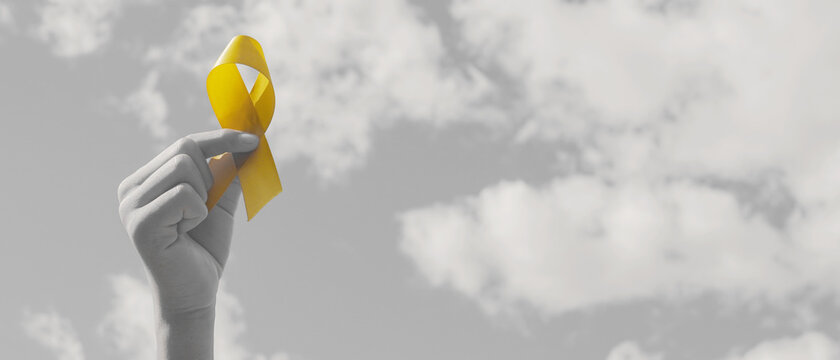 Hands holding yellow gold ribbon over  sky, Sarcoma Awareness, Bone cancer, childhood cancer awareness, September yellow, World Suicide Prevention Day concept